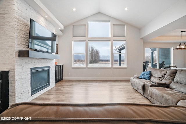 living area featuring high vaulted ceiling, wood finished floors, an inviting chandelier, a fireplace, and baseboards