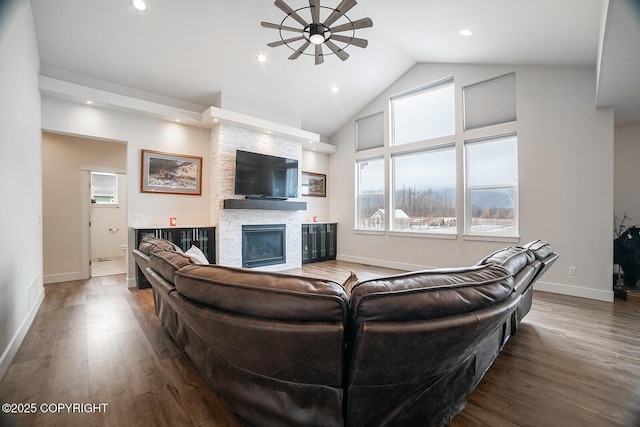 living area with a ceiling fan, wood finished floors, recessed lighting, a stone fireplace, and baseboards