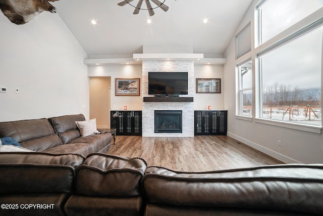 living area featuring baseboards, a stone fireplace, recessed lighting, wood finished floors, and high vaulted ceiling