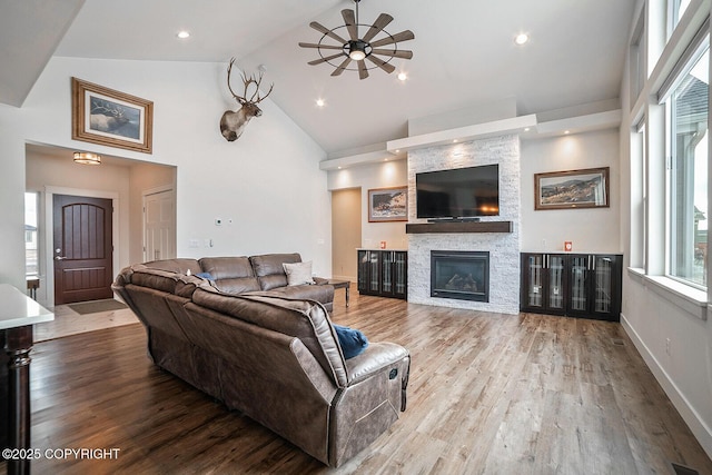 living room featuring a stone fireplace, high vaulted ceiling, a ceiling fan, and wood finished floors