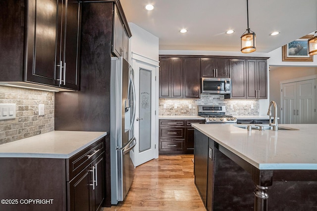 kitchen with decorative light fixtures, dark brown cabinetry, light wood-type flooring, stainless steel appliances, and a sink