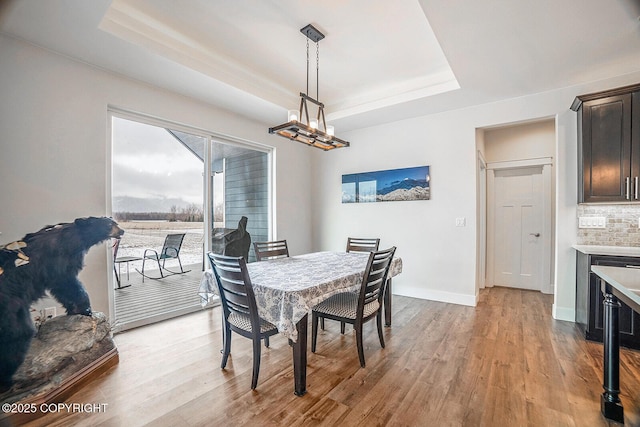 dining room featuring baseboards, a raised ceiling, wood finished floors, and a chandelier