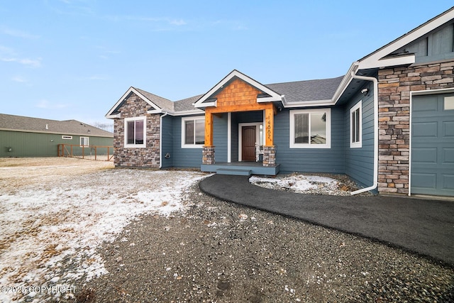 view of front of property featuring a garage, stone siding, roof with shingles, and fence