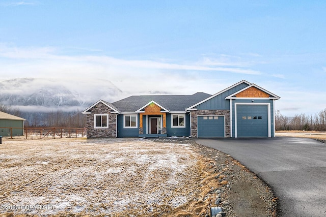 view of front of house with board and batten siding, fence, a garage, stone siding, and driveway