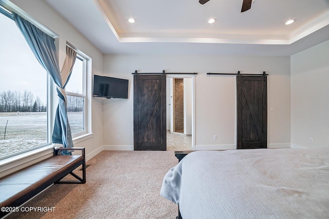 carpeted bedroom with a barn door, recessed lighting, baseboards, and a tray ceiling