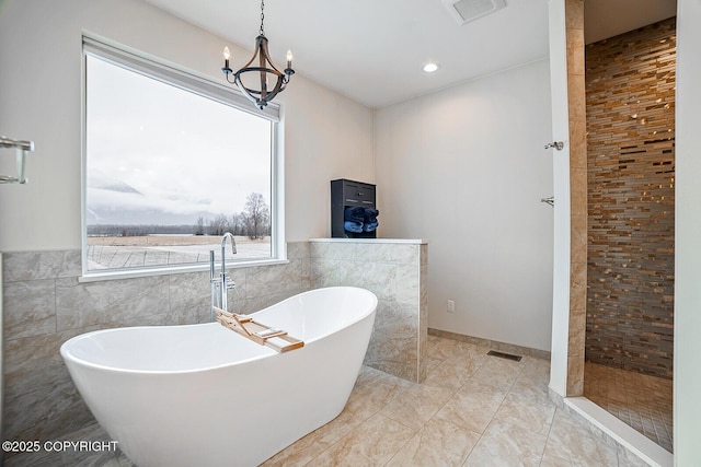 full bathroom featuring a soaking tub, visible vents, tile walls, and an inviting chandelier