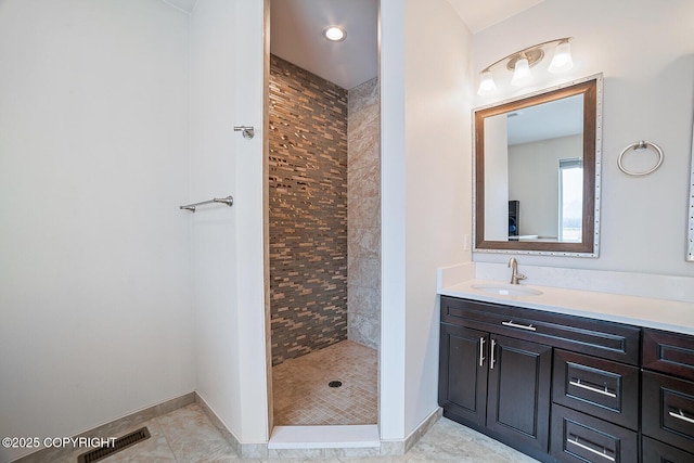 bathroom with vanity, baseboards, visible vents, a tile shower, and tile patterned floors