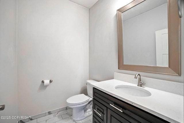 half bath with baseboards, toilet, marble finish floor, and vanity