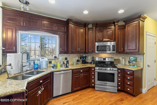 kitchen with tasteful backsplash, stainless steel appliances, a sink, light wood-style floors, and light stone countertops