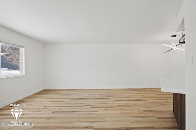 empty room featuring an inviting chandelier, baseboards, and light wood finished floors