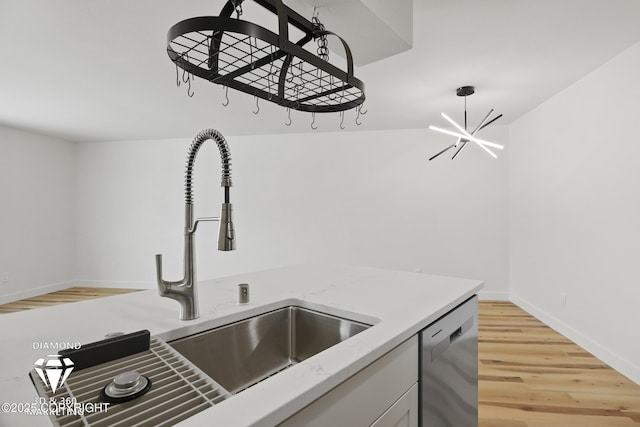 kitchen with dishwasher, light stone counters, light wood-style flooring, an inviting chandelier, and a sink