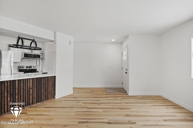 kitchen featuring baseboards, light wood-type flooring, decorative backsplash, white cabinets, and stainless steel appliances