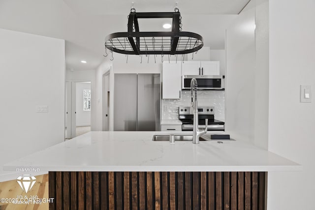 kitchen featuring tasteful backsplash, a peninsula, stainless steel appliances, white cabinetry, and a sink