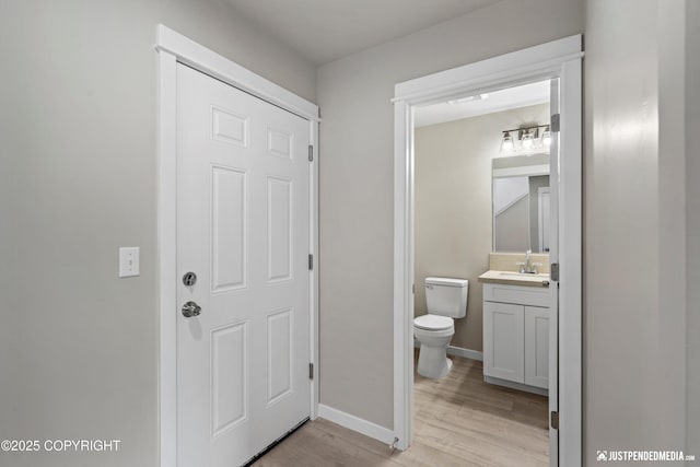 half bathroom featuring toilet, vanity, baseboards, and wood finished floors