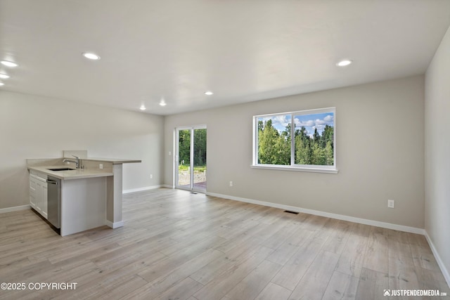 kitchen featuring visible vents, light wood-style flooring, a sink, stainless steel dishwasher, and light countertops