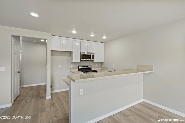 kitchen with light wood-type flooring, light countertops, a peninsula, white cabinets, and stainless steel appliances