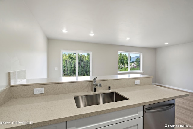 kitchen featuring light wood-type flooring, a sink, light stone counters, white cabinetry, and dishwasher