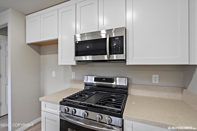 kitchen with white cabinetry, light stone countertops, baseboards, and appliances with stainless steel finishes