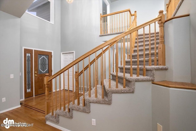 stairway featuring baseboards, a towering ceiling, and wood finished floors