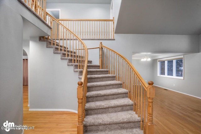 stairs with arched walkways, a notable chandelier, baseboards, and wood finished floors