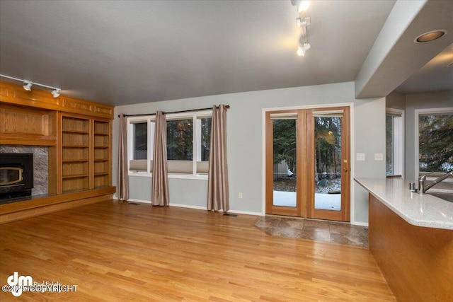 unfurnished living room featuring rail lighting, built in features, wood finished floors, and baseboards