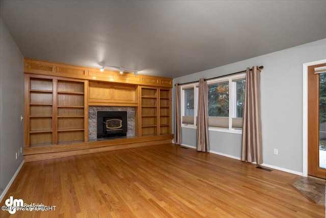 unfurnished living room with a wood stove, baseboards, visible vents, and light wood-type flooring