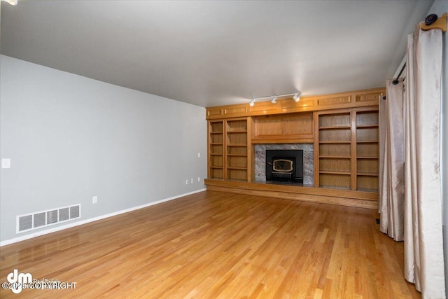 unfurnished living room with visible vents, baseboards, light wood-style floors, and rail lighting