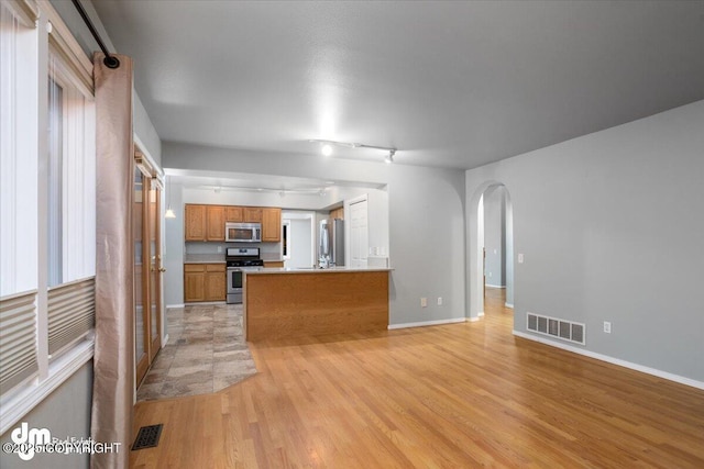 kitchen featuring visible vents, light wood finished floors, arched walkways, stainless steel appliances, and brown cabinets