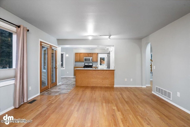 unfurnished living room featuring light wood-style floors, arched walkways, visible vents, and baseboards