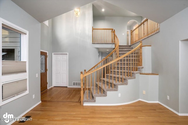 staircase with visible vents, a high ceiling, baseboards, and wood finished floors