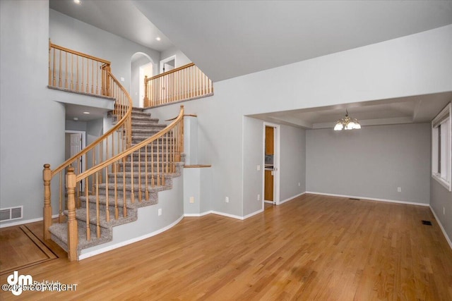 unfurnished living room with visible vents, a notable chandelier, wood finished floors, baseboards, and stairs