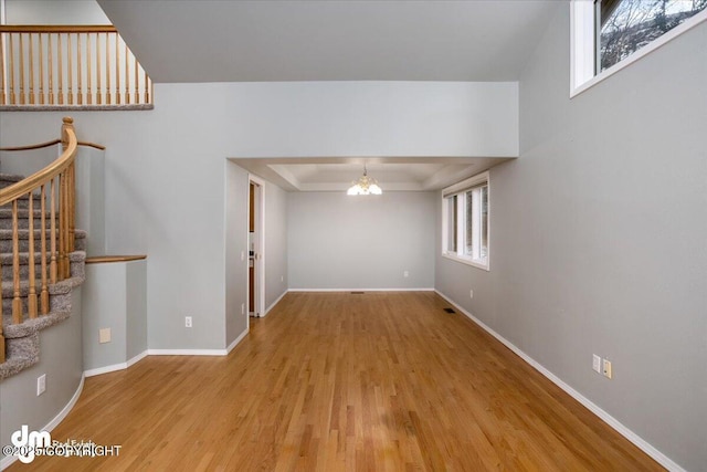 unfurnished living room with baseboards, stairway, a tray ceiling, an inviting chandelier, and wood finished floors