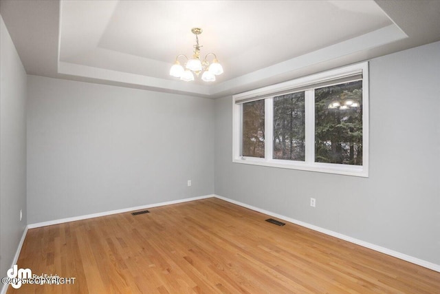 spare room featuring a chandelier, visible vents, a tray ceiling, and wood finished floors