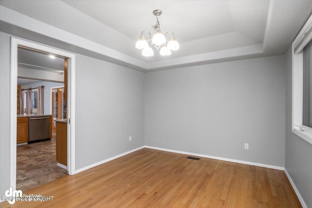 empty room featuring visible vents, light wood-type flooring, a raised ceiling, and an inviting chandelier