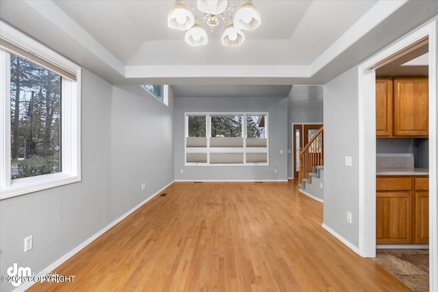 unfurnished living room featuring a wealth of natural light, stairway, a raised ceiling, and a notable chandelier