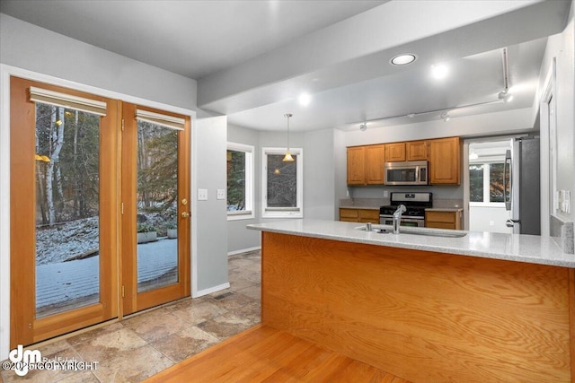 kitchen with brown cabinetry, a peninsula, plenty of natural light, light countertops, and appliances with stainless steel finishes