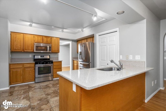 kitchen with a peninsula, brown cabinetry, appliances with stainless steel finishes, and a sink