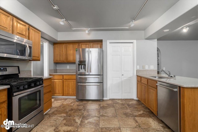 kitchen featuring brown cabinetry, arched walkways, a sink, stainless steel appliances, and light countertops