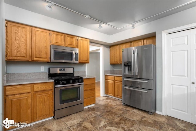 kitchen with brown cabinetry, track lighting, stainless steel appliances, and light countertops