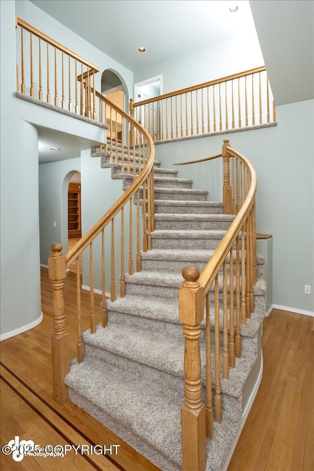 stairs with recessed lighting, baseboards, arched walkways, and wood finished floors