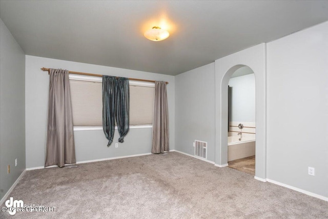 unfurnished bedroom with ensuite bath, visible vents, arched walkways, and carpet floors