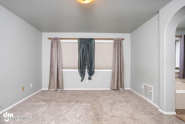 carpeted empty room with visible vents, arched walkways, and baseboards