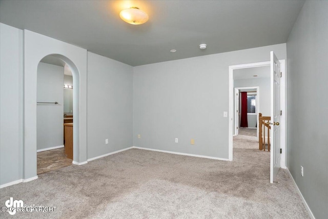 empty room featuring arched walkways, baseboards, and carpet