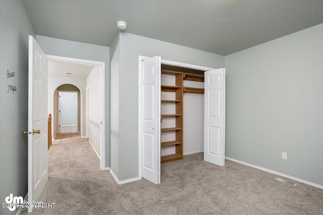 unfurnished bedroom with baseboards, visible vents, arched walkways, and carpet floors