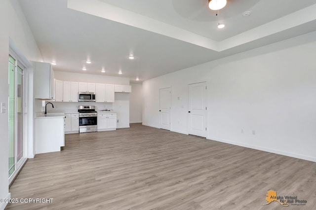 kitchen featuring open floor plan, light countertops, light wood-style flooring, appliances with stainless steel finishes, and a sink