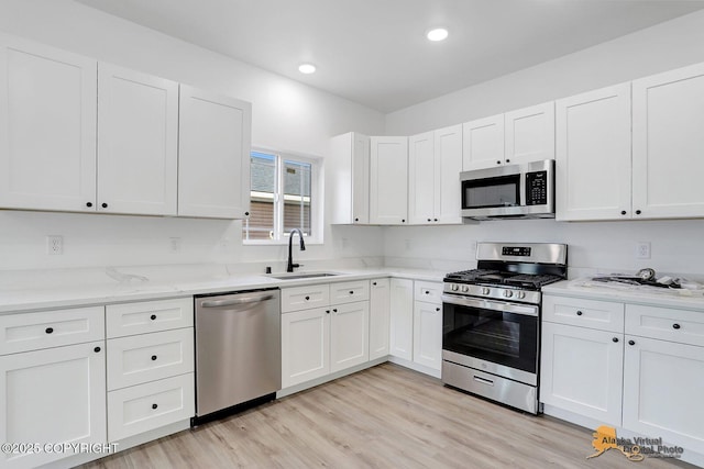 kitchen with white cabinets, appliances with stainless steel finishes, light wood-style floors, and a sink