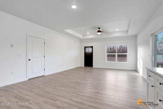 unfurnished living room with light wood-style flooring, a ceiling fan, a tray ceiling, recessed lighting, and baseboards