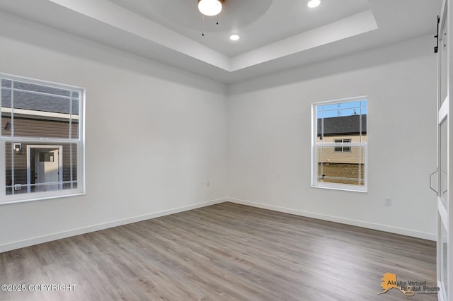 empty room with a tray ceiling, wood finished floors, and baseboards