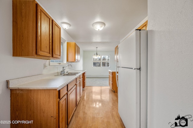 kitchen featuring brown cabinets, a sink, freestanding refrigerator, light countertops, and a baseboard radiator