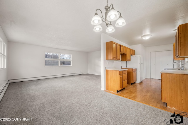 kitchen with a baseboard heating unit, light countertops, freestanding refrigerator, an inviting chandelier, and a sink